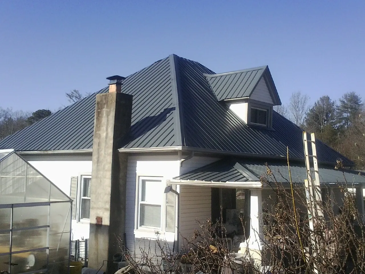 Dark blue standing seam metal roof on a white farmhouse with dormer — Slate & Tile Roof Repair by Roofing Brothers in Bradyville
