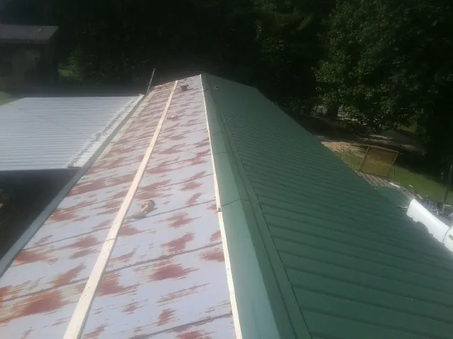 Old rusted panels beside newly installed green metal roofing — Wind Damage Roof Repair by Roofing Brothers in Bradyville