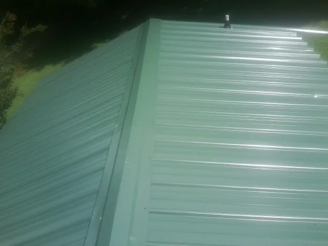 New green metal panels meeting at the ridge of a roof — Flat Roof Repair work by our crew in Bradyville