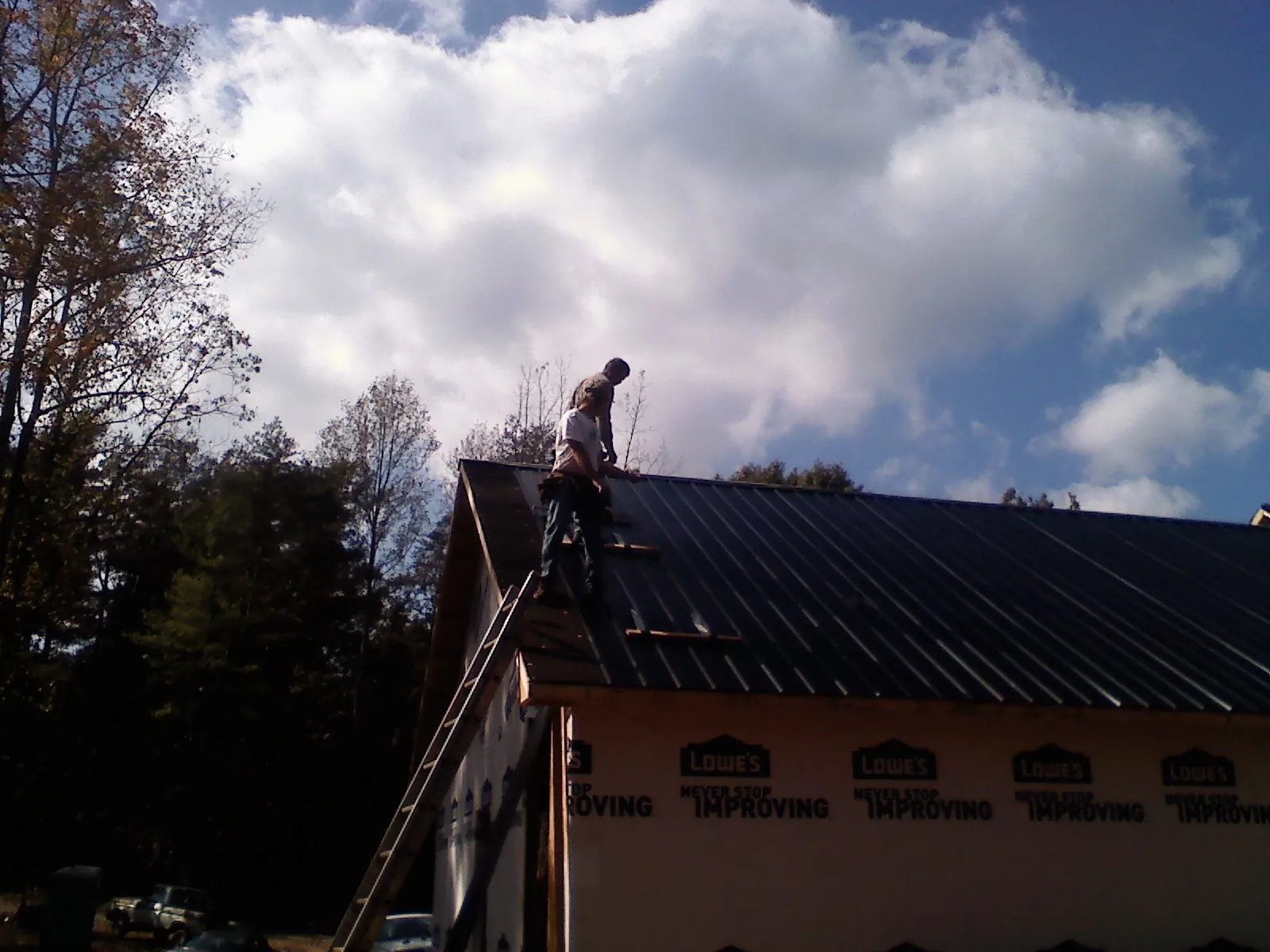 Roofer fastening dark metal panels high against a cloudy sky, from a Roof Inspection job in Bradyville