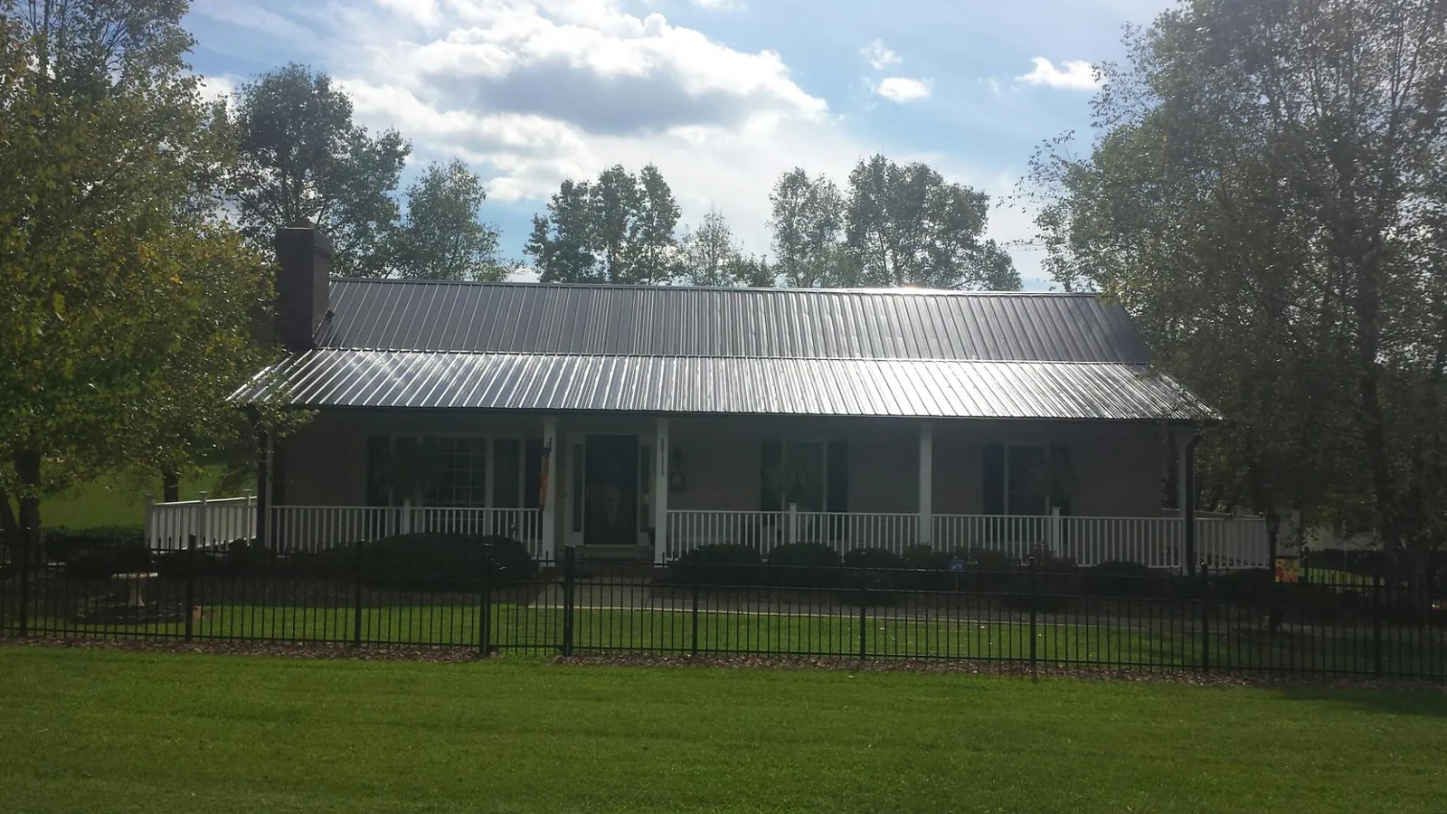 Gray metal roof on a brick ranch with a full width front porch — Gutter Guard Installation work by our crew in Bradyville