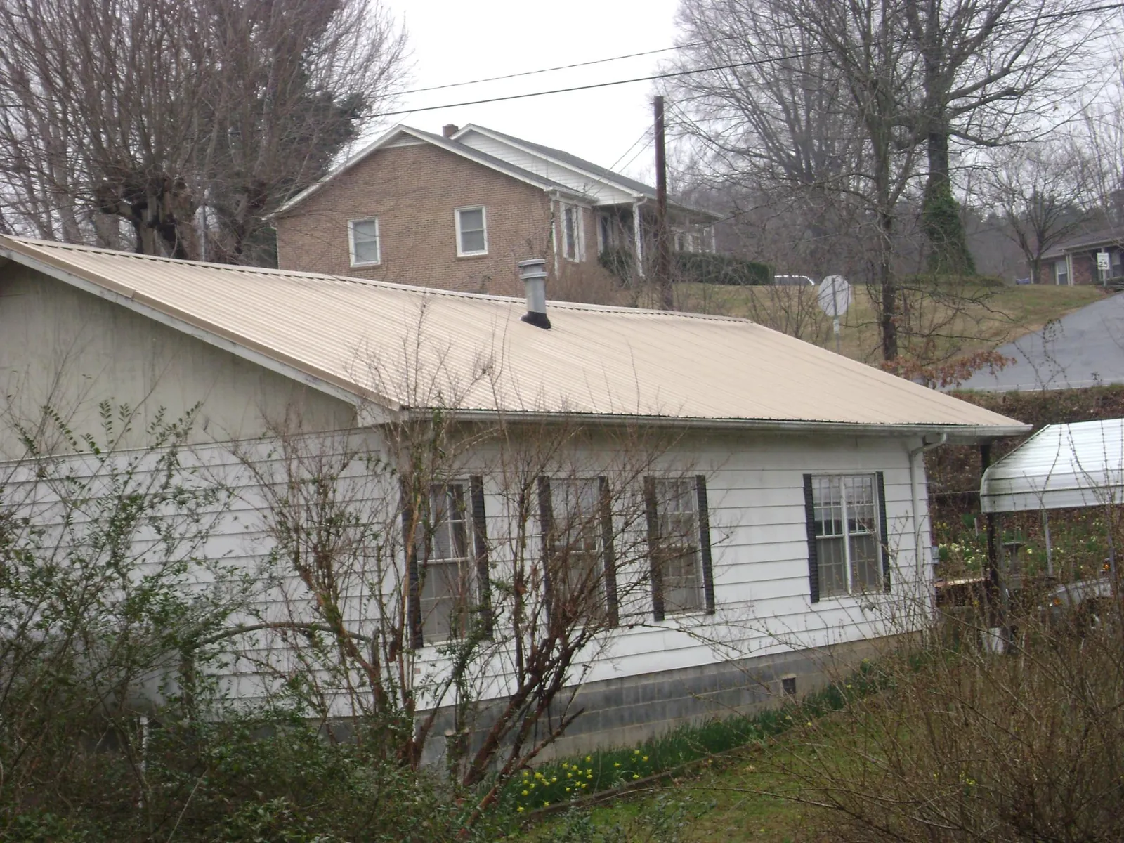 Tan metal roof on a white sided house set into a hillside — Commercial Roofing by Roofing Brothers in Bradyville