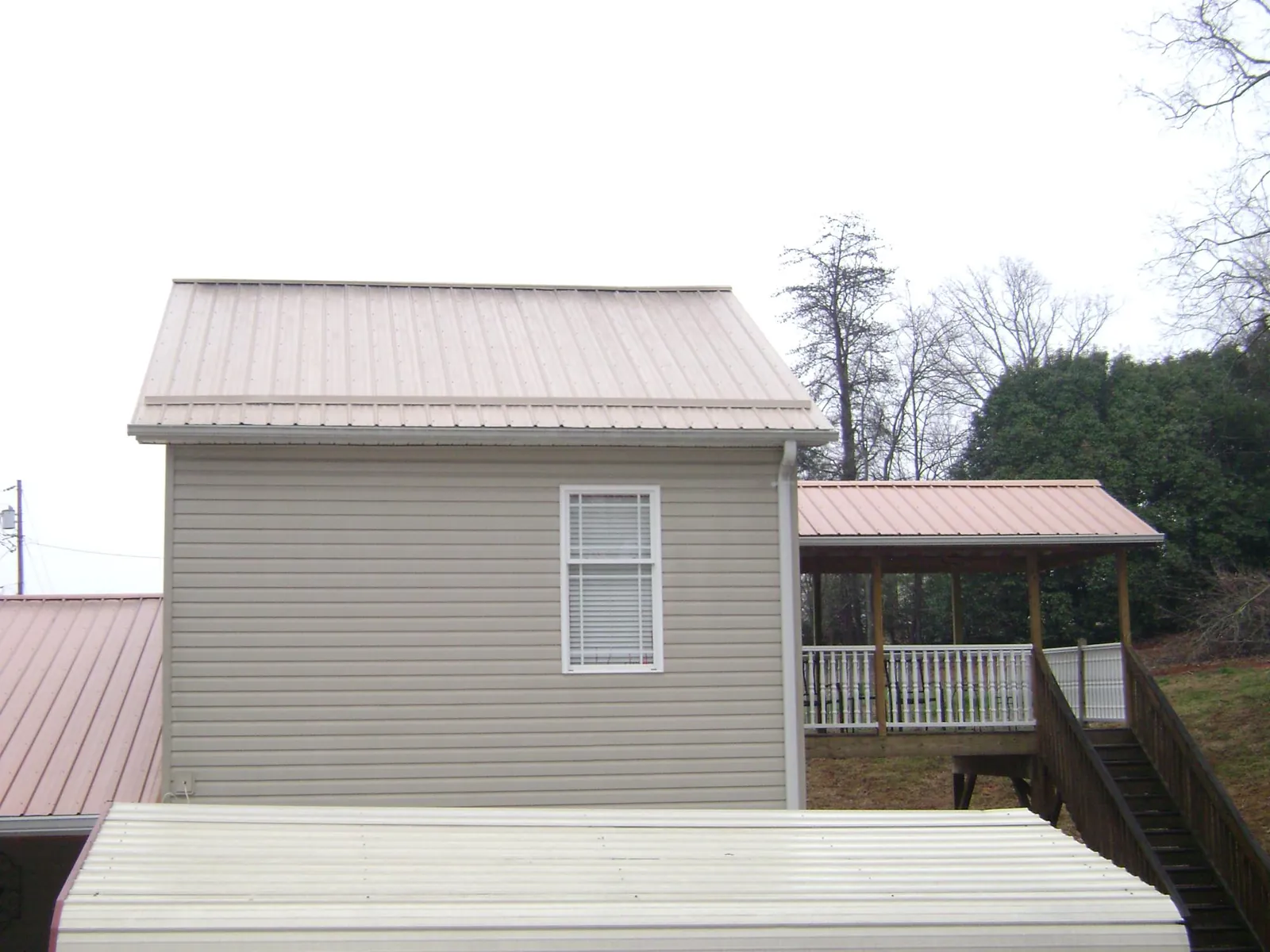 Tan metal roofs on a two story addition and attached porch, from a Roof Replacement job in Bradyville